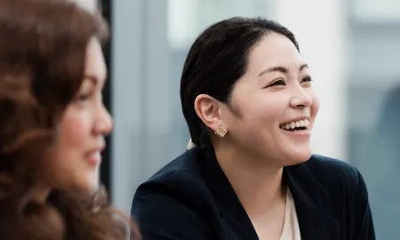 Close-up of a smiling woman in a navy blazer attentively listening during an in-person business school event.