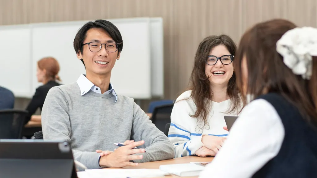 Smiling business school students engaged in a group discussion at a table with tablets and papers.